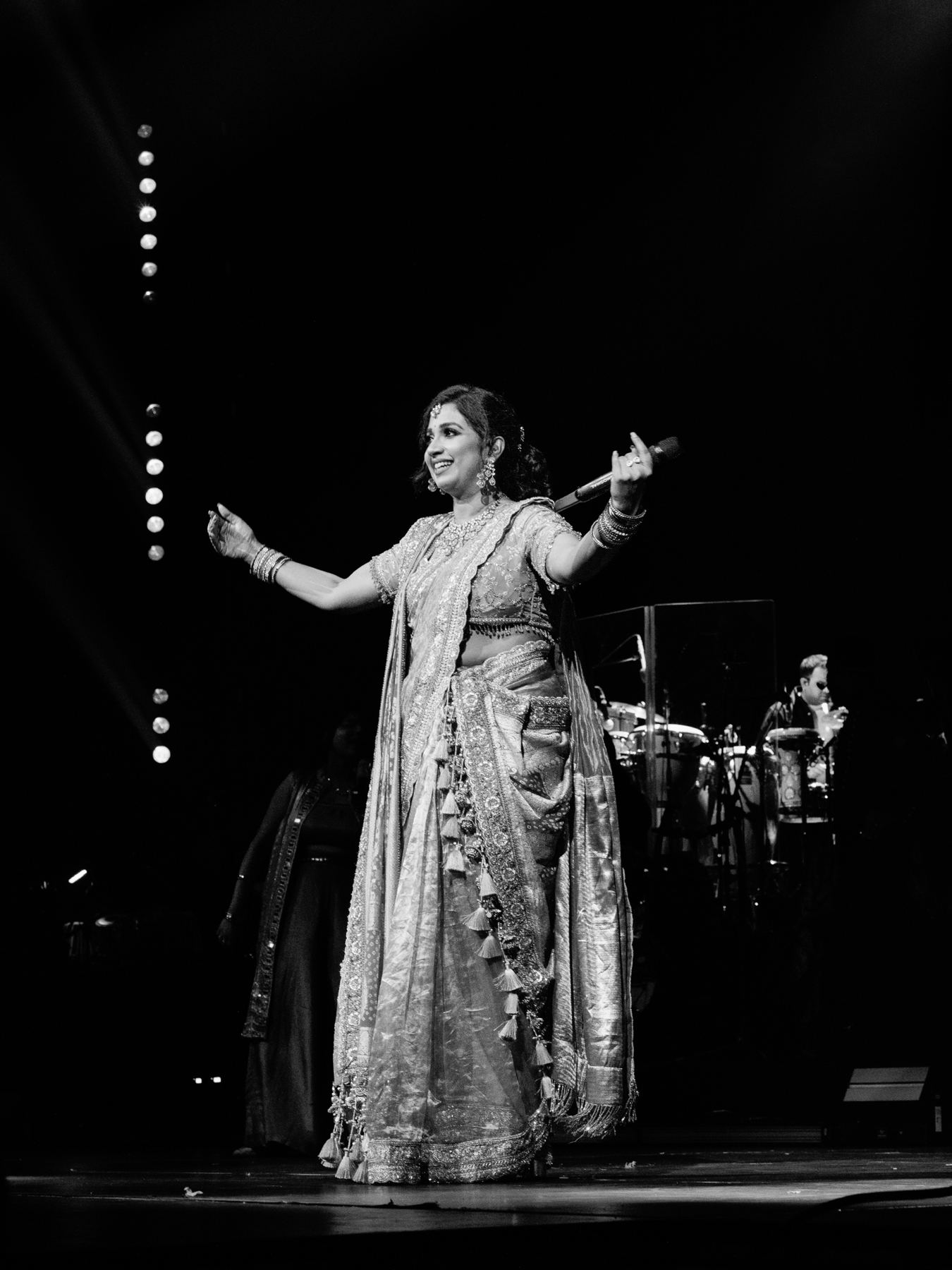Singer in an embroidered saree with arms open, band behind her