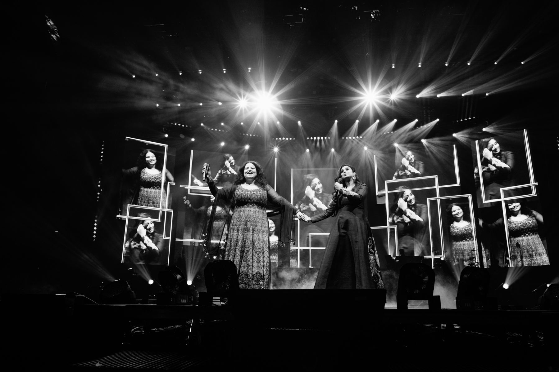 Two singers holding hands in front of video screens and starburst stage lights